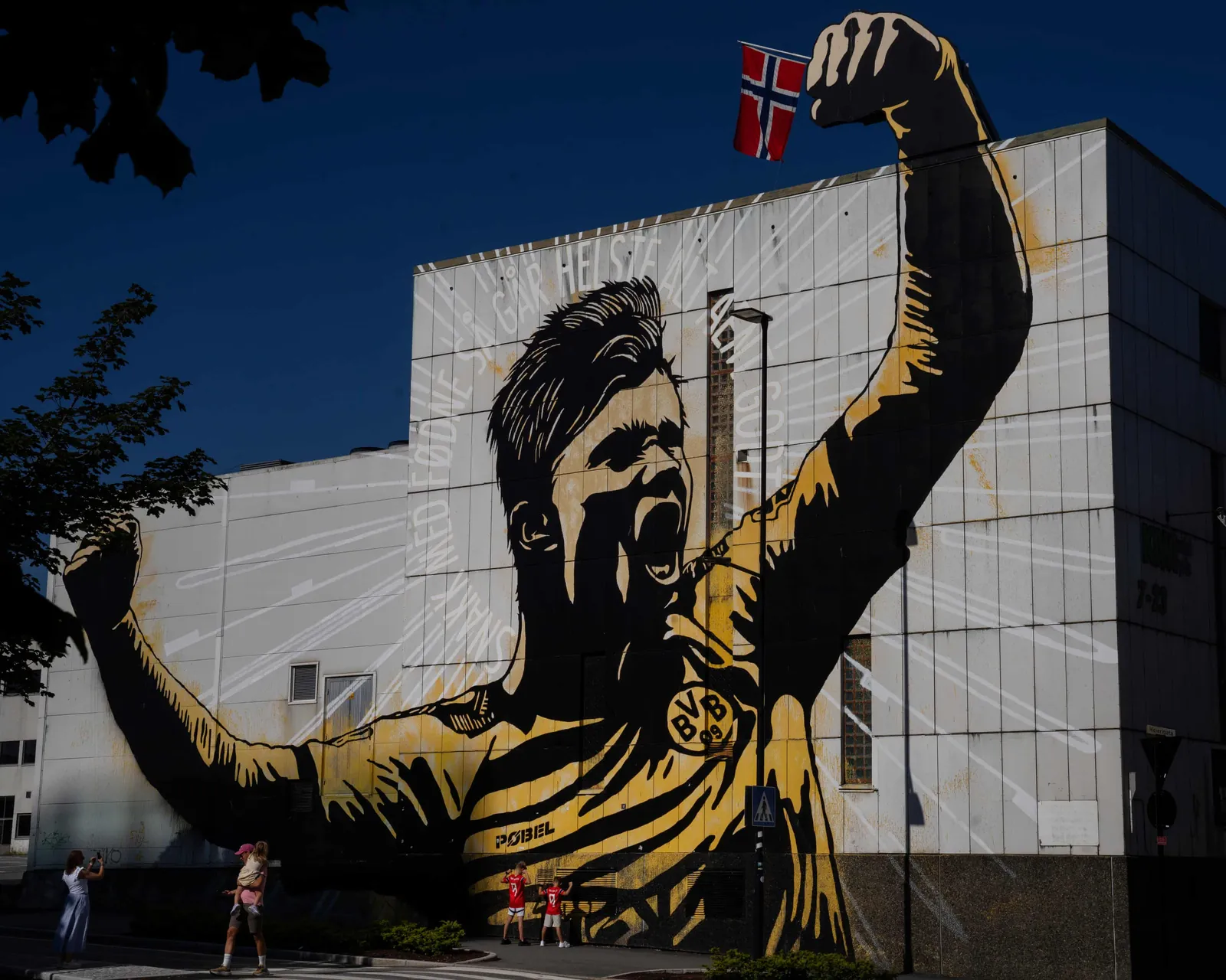 A large mural of Haaland celebrating in yellow and black stripes covers the side of a white building